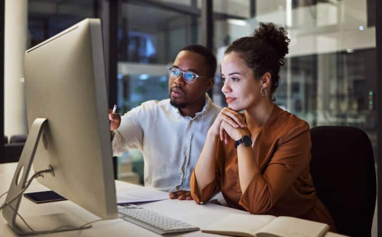 Business training, night planning and employees talking about corporate proposal on internet in dark office at night. African workers working on partnership on the web with computer during overtime